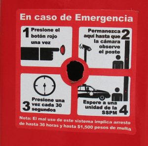 Instructional sign posted on red background with hole where button should be. 1. Press the red button once 2. Stay here until the camera sees the post 3. Press once every 30 seconds 4. Wait until the SSPM unit arrives.