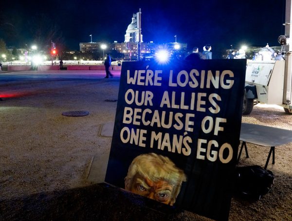 A sign that reads "WE'RE LOSING OUR ALLIES BECAUSE OF ONE MAN'S EGO" Along with a picture showing half of President Trump's face below the text