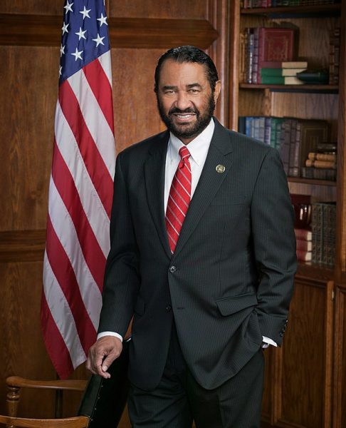 Representative Al Green posing for a portrait. He is wearing a black suit with a red striped tie. An American flag is pictured behind him.