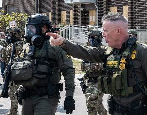 Paul Bovino pointing off camera with ICE officials in uniform beside him