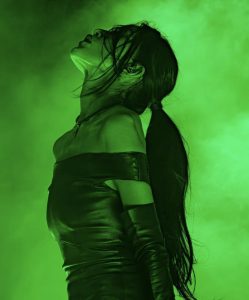 Artist Mariqueen Maandig onstage underneath a vibrant green light and smoke