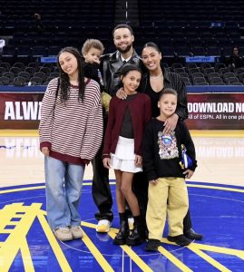Warriors player, Steph Curry, posing with family, on the court. Screenshot from an Instagram post. 