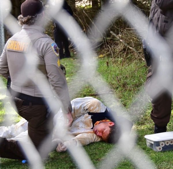 A picture of a man in a white suit being pepper sprayed, he is lying down on the ground with his eyes closed.